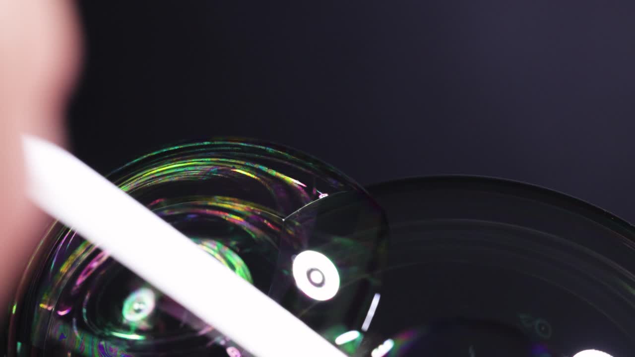 Close-up of soap bubbles reflecting colorful light patterns in a dark environment, highlighting surface tension and fluid dynamics