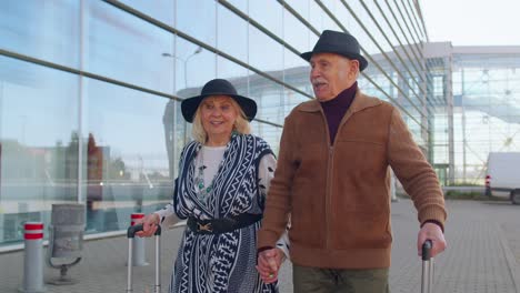 elderly husband wife retirees tourists go to airport terminal for boarding with luggage on wheels