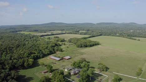 4k wide aerial view of farmhouse and surrounding fields with hills in distance