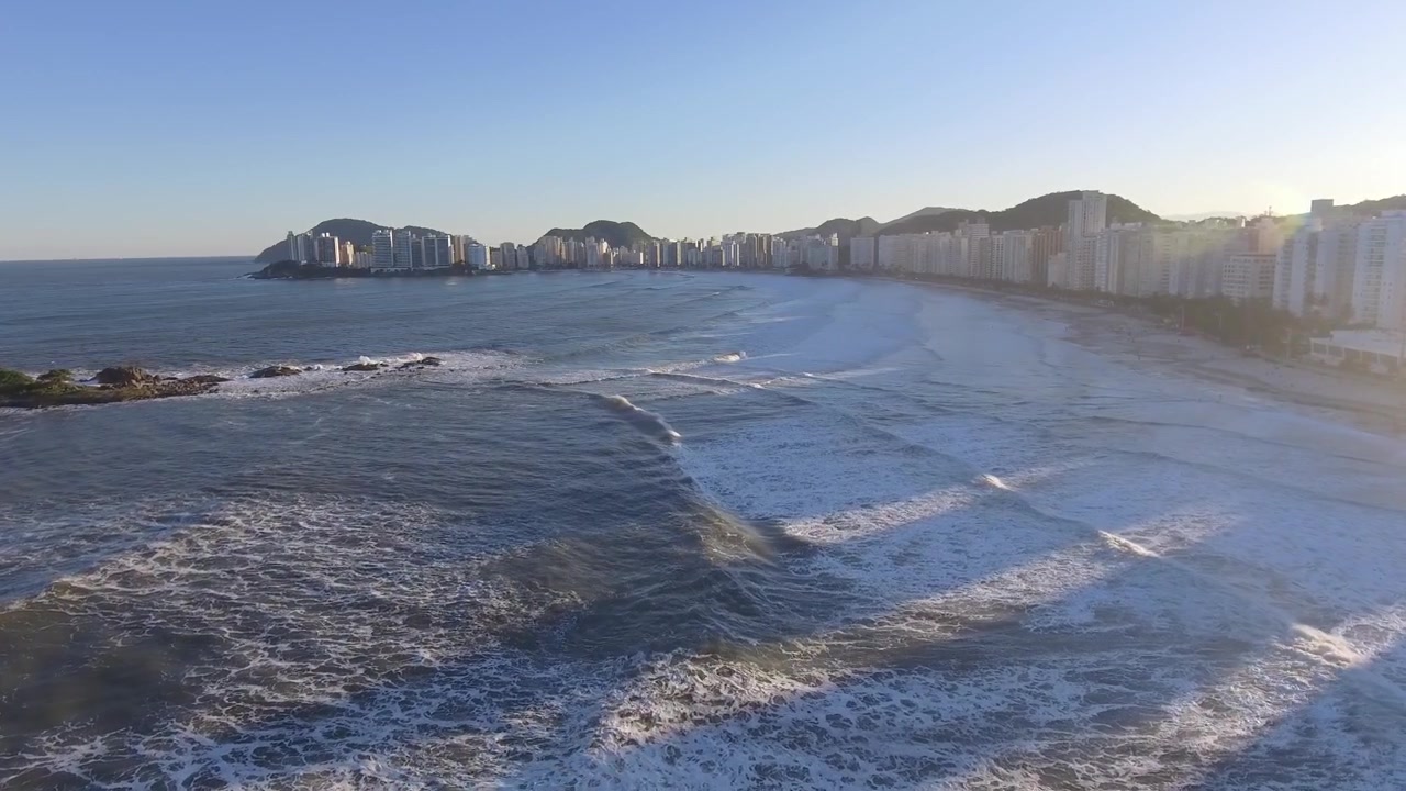 Imagens aéreas vibrantes de drone de Pitangueiras, Guarujá, Brasil, ao pôr do sol. A praia se estende ao longo da costa, capturada com detalhes impressionantes de cima.