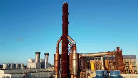 rising drone shot of power station chimney against bright blue sky