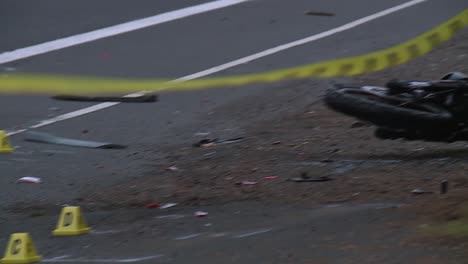 panning shot of skid marks to motorcycle crash behind police tape