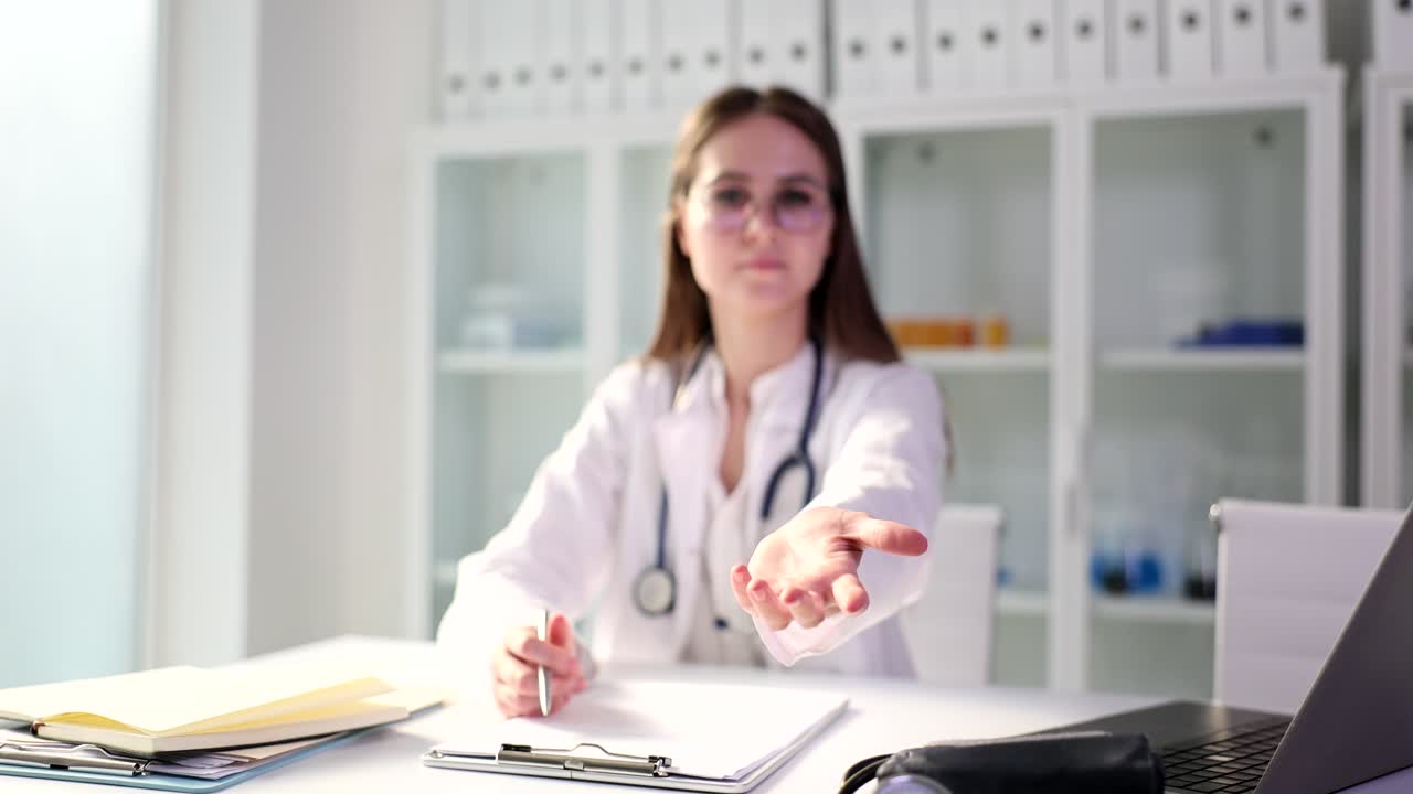 Young doctor in glasses stretches out hand offering help