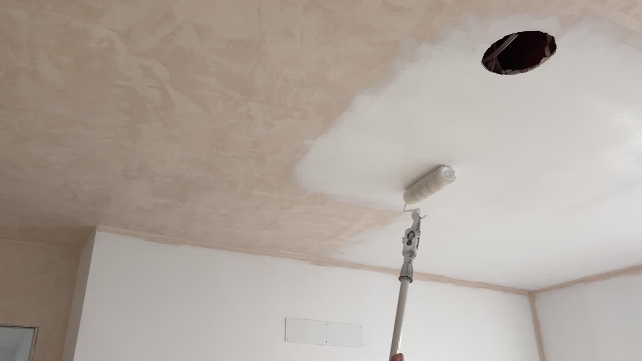 Una persona sta usando un rullo da pittura e applicando vernice alla superficie del soffitto; un imbianchino responsabile della pittura e decorazione di edifici.