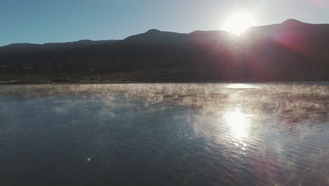 Aerial-Push-Pan-Over-Water-Toward-Desert-Mountain-Landscape-And-Sunset-In-The-Distance