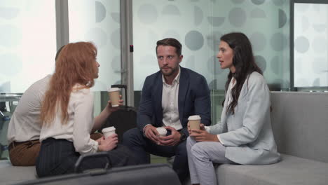 a working group of two businesswomen and two businessmen chatting relaxedly with some coffees in the lobby of an airport before a business trip 5