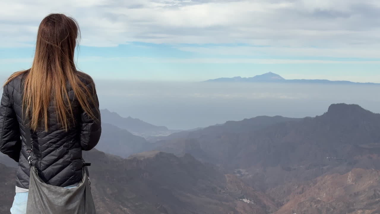 A woman with her back turned admires the beauty of Mount Teide from the Roque Nublo Natural Park on the island of Gran Canaria.