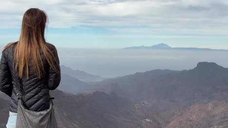 a woman with her back turned admires the beauty of mount teide from the roque nublo natural park on the island of gran canaria.