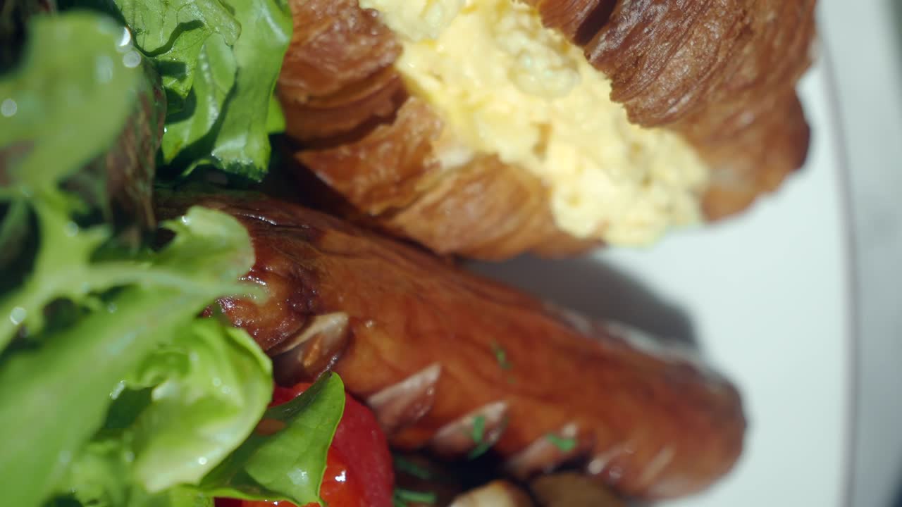 Close-up of a Breakfast Plate with Sausage, Mushrooms, Tomatoes, Lettuce, and Croissant with Scrambled Eggs