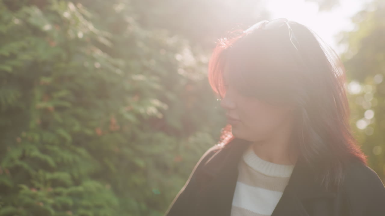 선글라스를 머리에 얹고 겨울 코트를 입은 여성이 공원 산책로를 따라 걷고 있어요. 손은 가을 단풍 위로 스치듯 움직이고, 따뜻한 햇살 아래 푸른 잎을 바라보며 조용히 명상하며 산책하고 있어요.