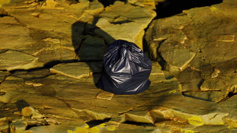 black trash bag lay on a rocky beach