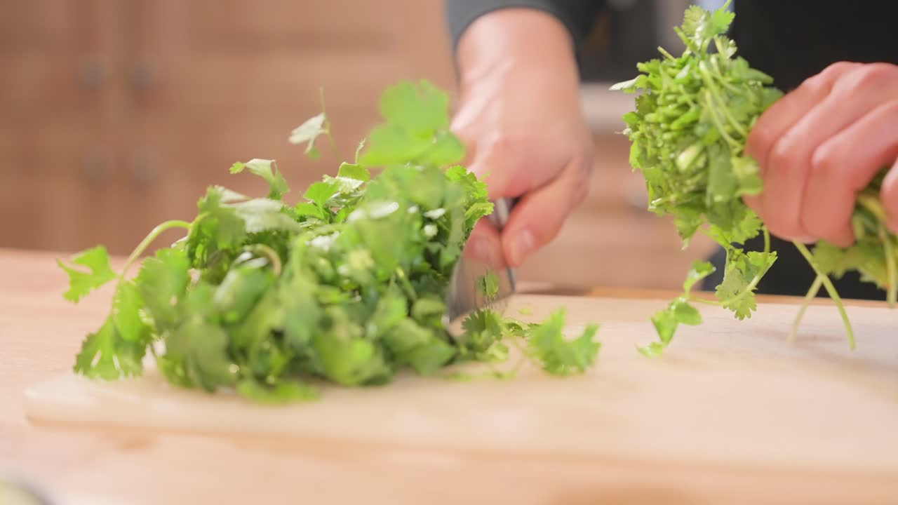 An at-home cook chops a bunch of cilantro in half, slicing through to separate the stems from the leafy tops.