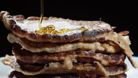 close up of syrup being poured onto stack of pancakes with icing sugar