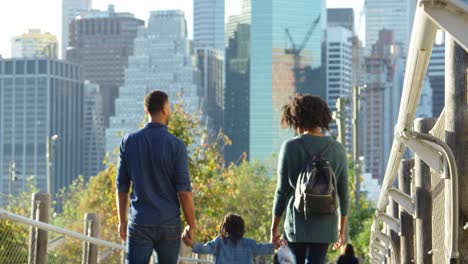 Couple-with-young-daughter-walking-on-footbridge,-back-view