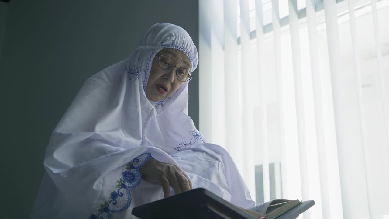 창문 근처에서 꾸란을 읽는 노인 여성