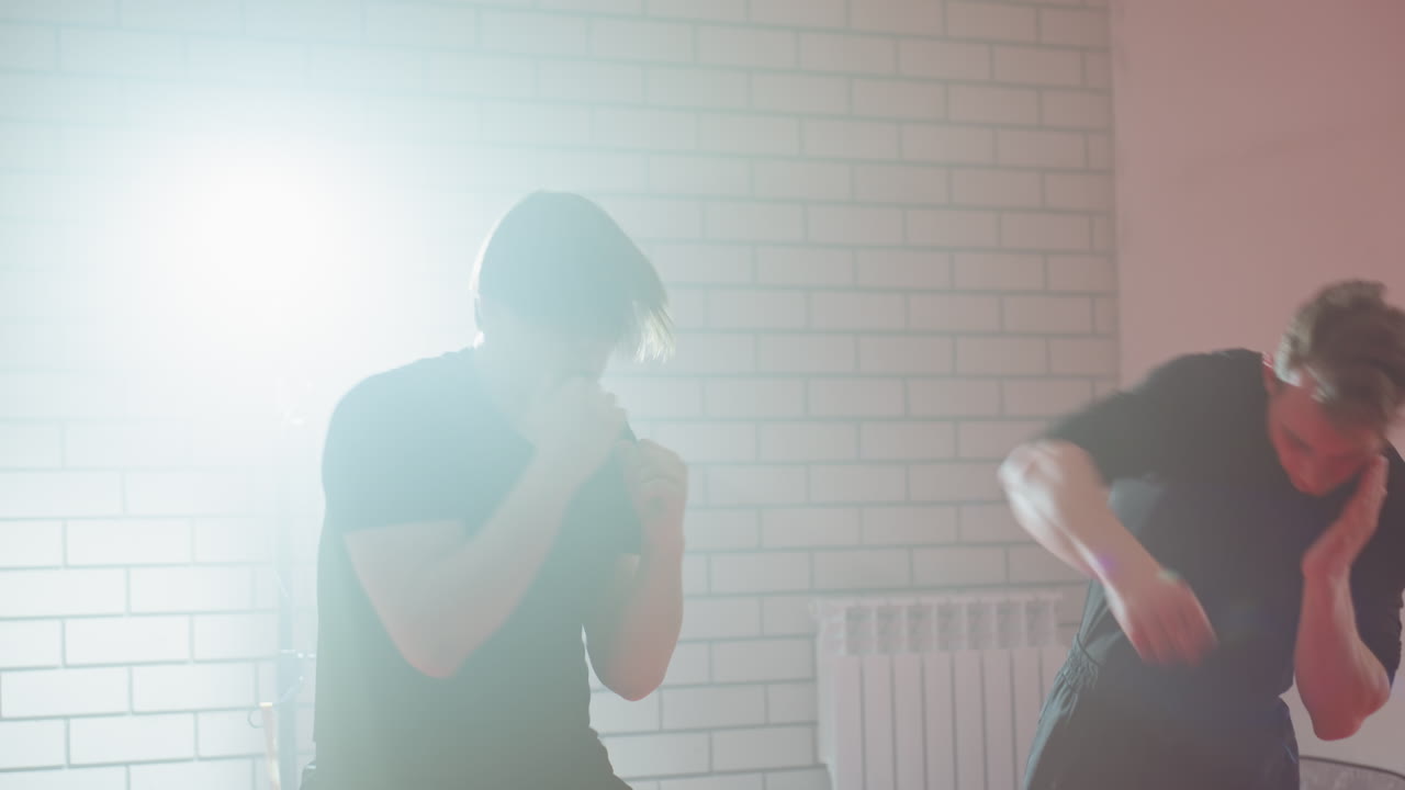 Boxers engaged in sparring session inside gym, wearing black training clothes, practicing punches and defense moves with focus and intensity, illuminated by bright light, showcasing energy, athletic