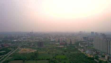 aerial drone shot flying forward over sunset cityscape with skyscraper multistory buildings and green fields