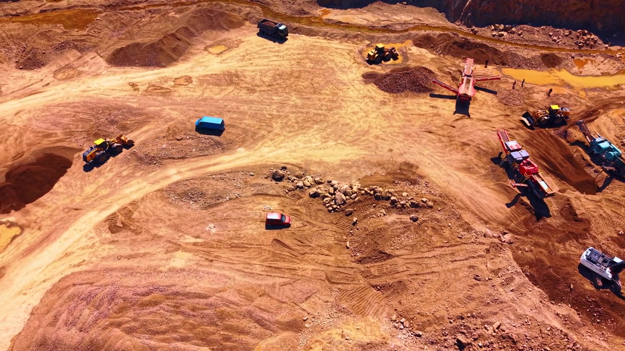 Aerial view of open pit stone quarry operation. Top view of heavy machinery working on brown sandy ground under bright daylight.