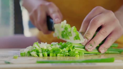 female cook chopping a bunch of fresh green onions on a wooden cutting board