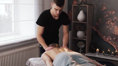 A-male-masseur-massages-a-young-woman's-back