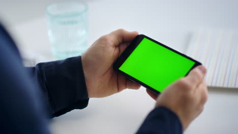 Close-up-man-hands-holding-smartphone-with-green-screen.-Male-looking-cell-phone