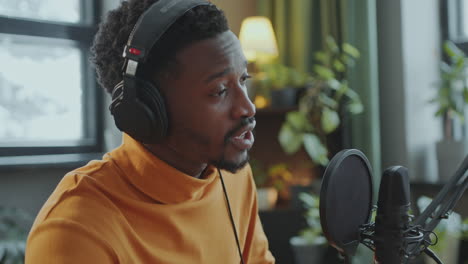 podcast host walking in studio, sitting at desk and recording new episode