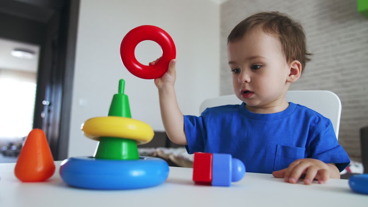 Lovely child assembling the colorful pyramid. Dark-haired kid puts on the rings from a toy on little hands.