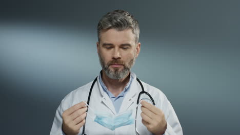 good looking man surgeon taking on blue mask when getting ready for the surgery on gray wall background