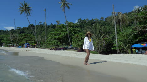 woman in a white dress walking on the shore of a beach
