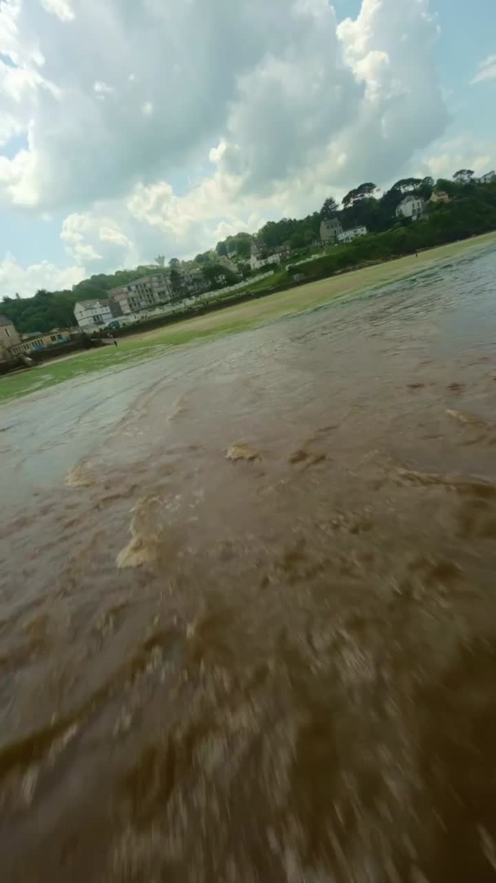 Ris Beach, Brittany, France - Shallow Waves Glide Over the Sand as a Line of Homes Sits Quietly on the Green Hillside Beneath a Bright, Cloud-streaked Sky - Vertical Shot