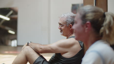 cheerful senior man having break after dancing in ballroom with his friends, and drinking water