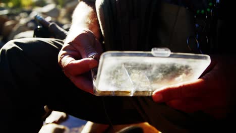 pescador con mosca quitando el cebo de la caja de aparejos