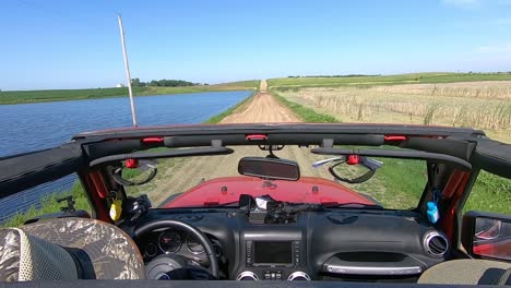 pov driving on a flooded graveled road in rural south dakota between a flooded pond and marsh area