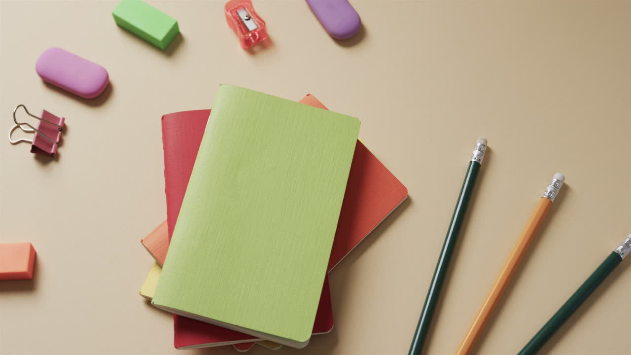 Close up of colourful notebooks with school stationery on beige background, in slow motion