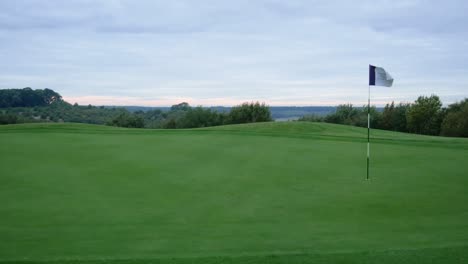 Toma-4k-De-Un-Campo-De-Golf-Verde-Y-Bandera-Al-Amanecer