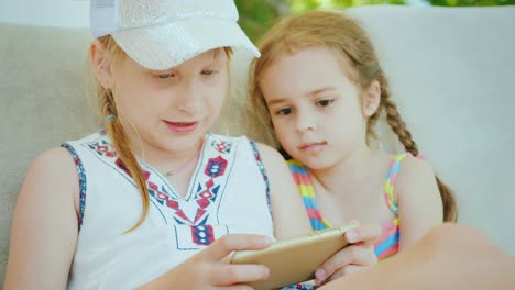 dos chicas geniales están jugando al teléfono en un complejo marítimo, sentadas en una hamaca cerca de la piscina
