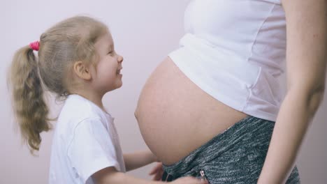 girl-laughs-playing-with-pregnant-mom-belly-in-light-room