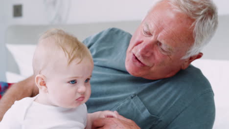 grandfather lying in bed at home looking after baby grandson