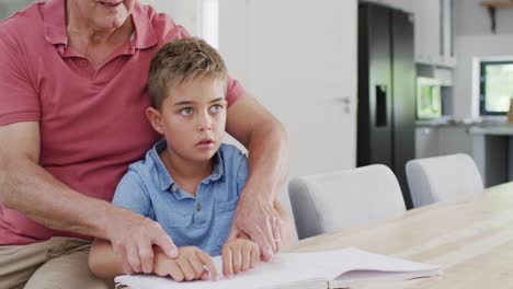 Glücklicher-Kaukasischer-Großvater-Und-Enkel-Sitzen-Am-Tisch-Und-Lesen-Blindenschrift,-Zeitlupe