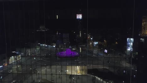 an evening hd aerial shot showing reflection of a colorful fountain and a city square in a corporate glass building