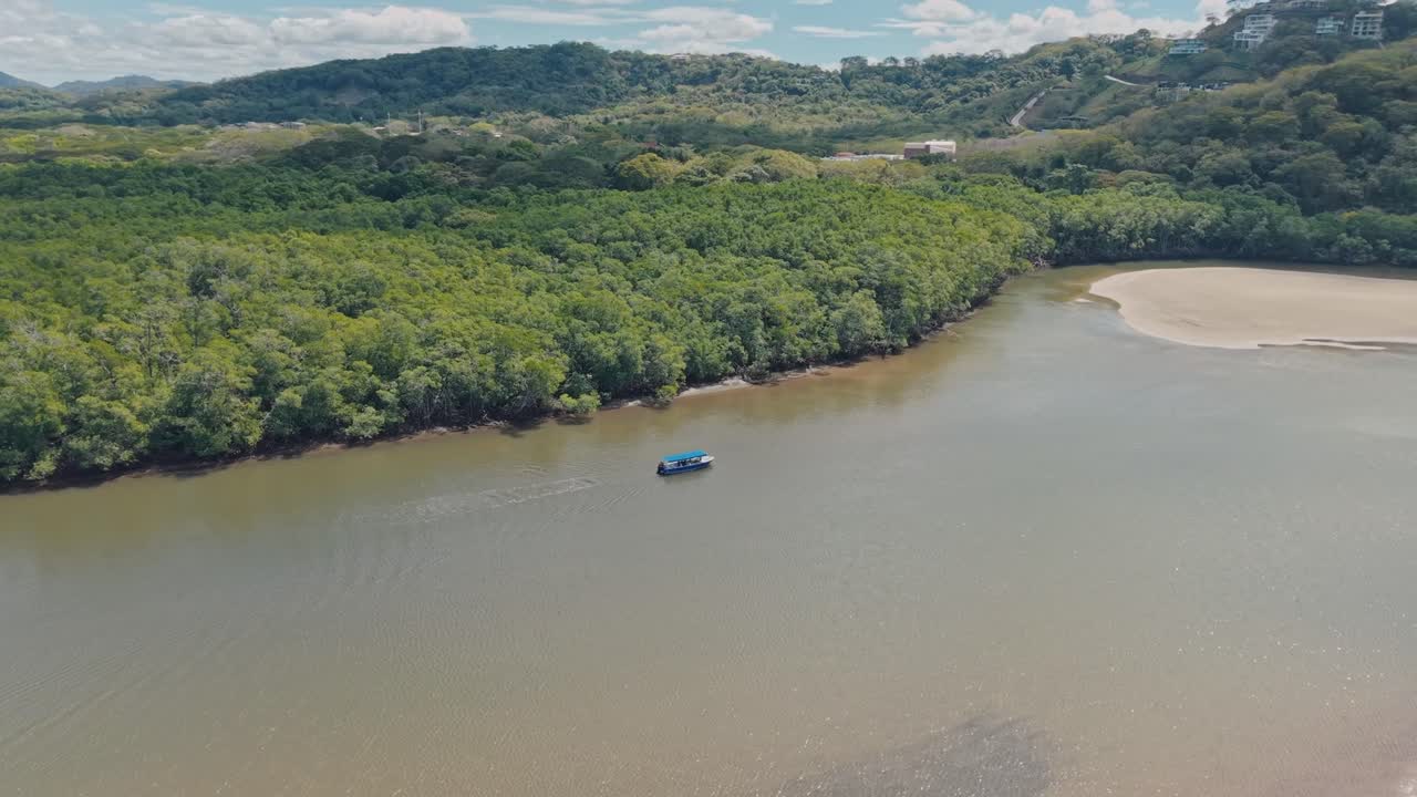 Aerial zoom-in of a boat navigating calm shallow waters surrounded by dense mangroves.