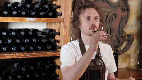 authentic shot of successful male sommelier is tasting a flavor and checking white wine quality poured in transparent glass in a wine cellar.