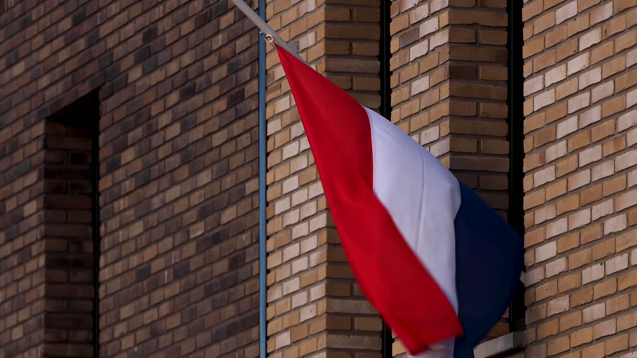 바람에 날리는 네덜란드 국기 클로즈업 반기둥이 전시장에서 쓰러진 사람들을 추모하기 위해 현대식 건물의 외관을 쓰다듬고 있다