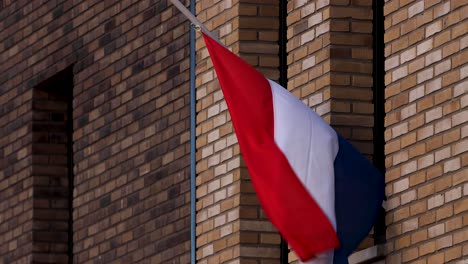 dutch national flag closeup blowing in the wind hanging half mast stroking the exterior facade of a modern building in commemoration of those fallen in war times