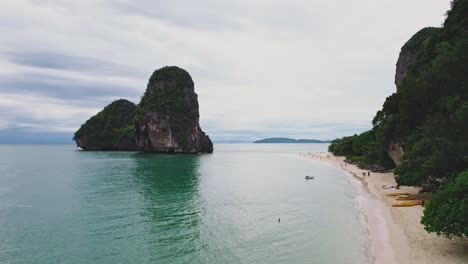 Playa-De-Phra-Nang-Con-Turistas-Caminando-Por-La-Arena-Con-Islas-De-Piedra-Caliza-Sobresaliendo-Del-Mar-De-Andamán