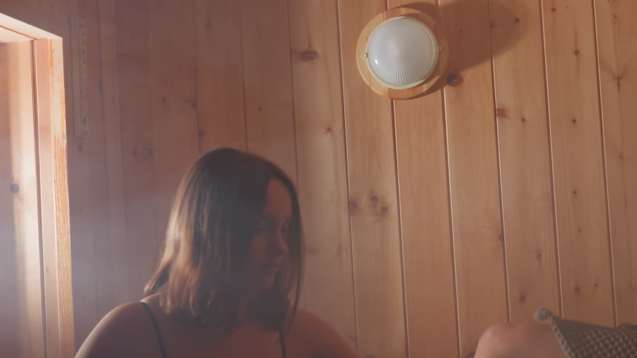 Young woman in sauna room with steam enjoying relaxing moment, holding towel and enjoying peaceful atmosphere, glowing light illuminating wooden walls, spa wellness and relaxation concept