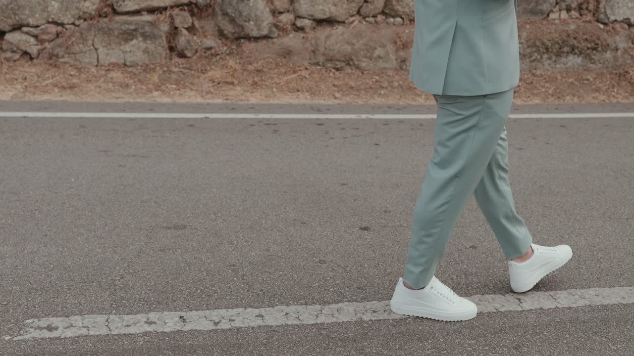 Pria elegan berjas pastel berjalan di jalan aspal