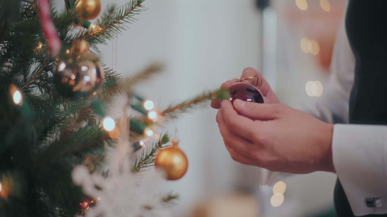 hombre sosteniendo una bola de vidrio roja por el árbol de navidad