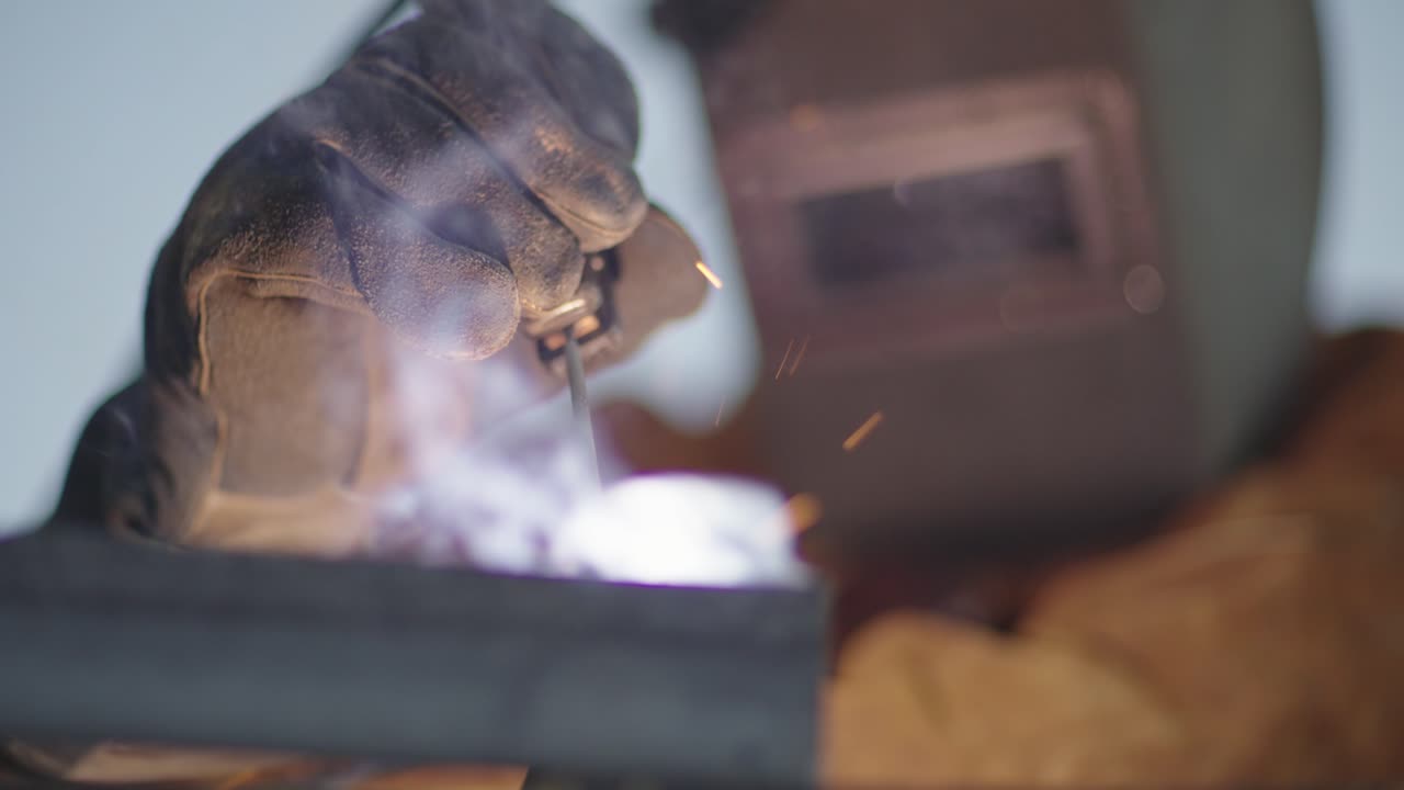 Saldatura in slow motion, scintille e fumo, primo piano del guanto dell'operaio.