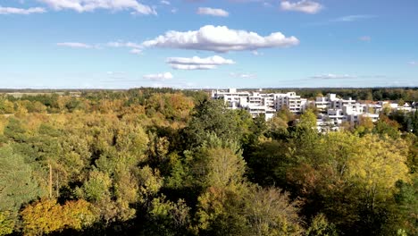 Aerial-view-over-Munich-suburbs:-Drone-glides-showcasing-crisp-autumn-forests-leading-to-majestic-mountain-backdrops,-an-urban-natural-harmony